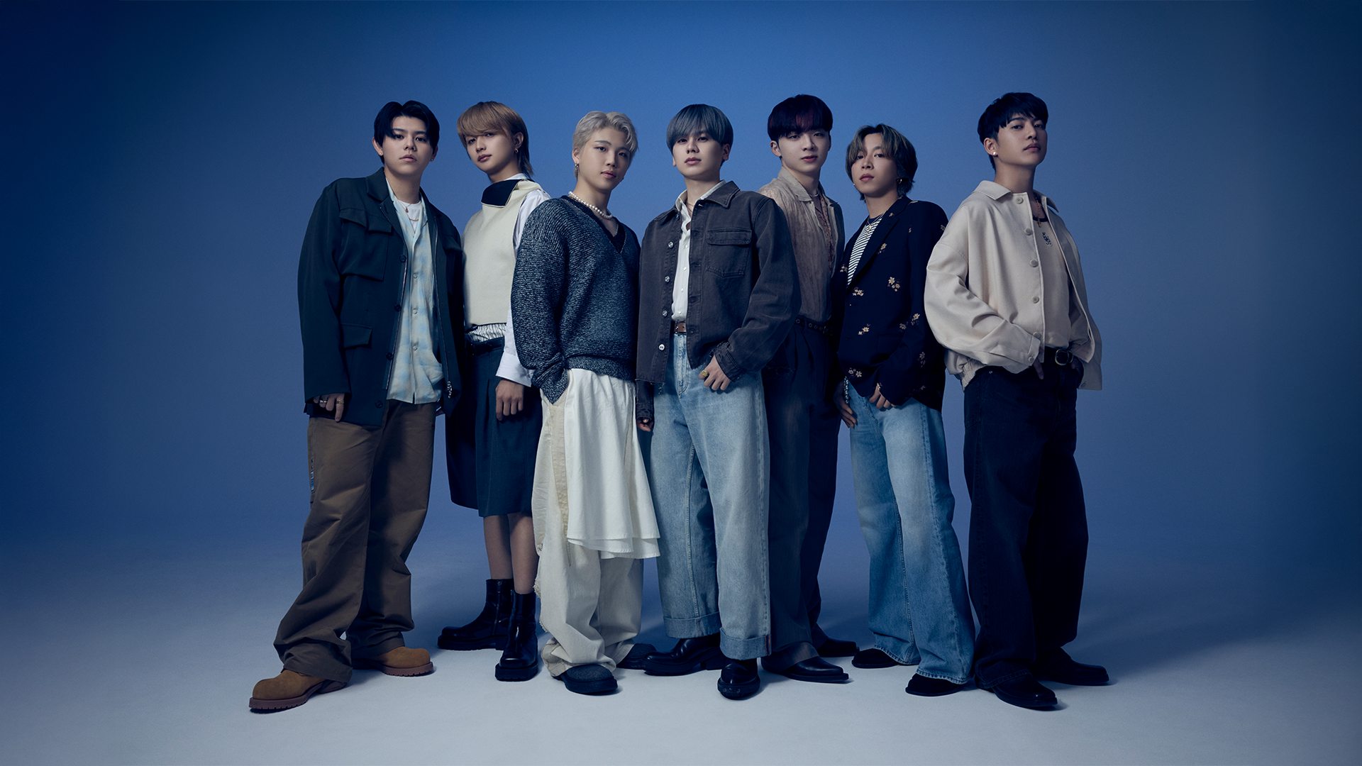 7 人のスタイリッシュな若い男性が、それぞれユニークでモダンな服を着て、青いグラデーションの背景に対して自信に満ちたポーズをとっています。